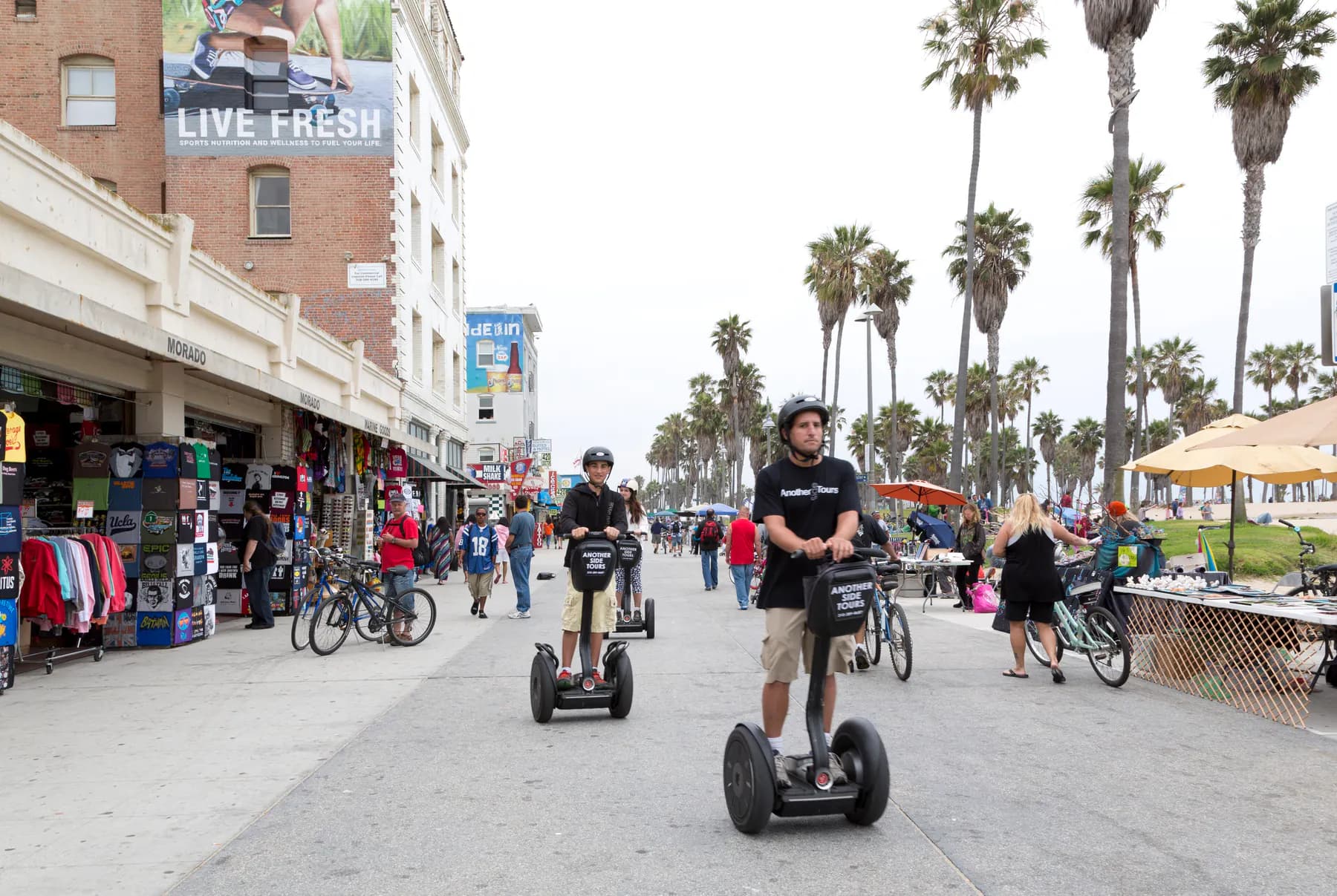 People walking and cycling along the Venice boardwalk beside shops and public space